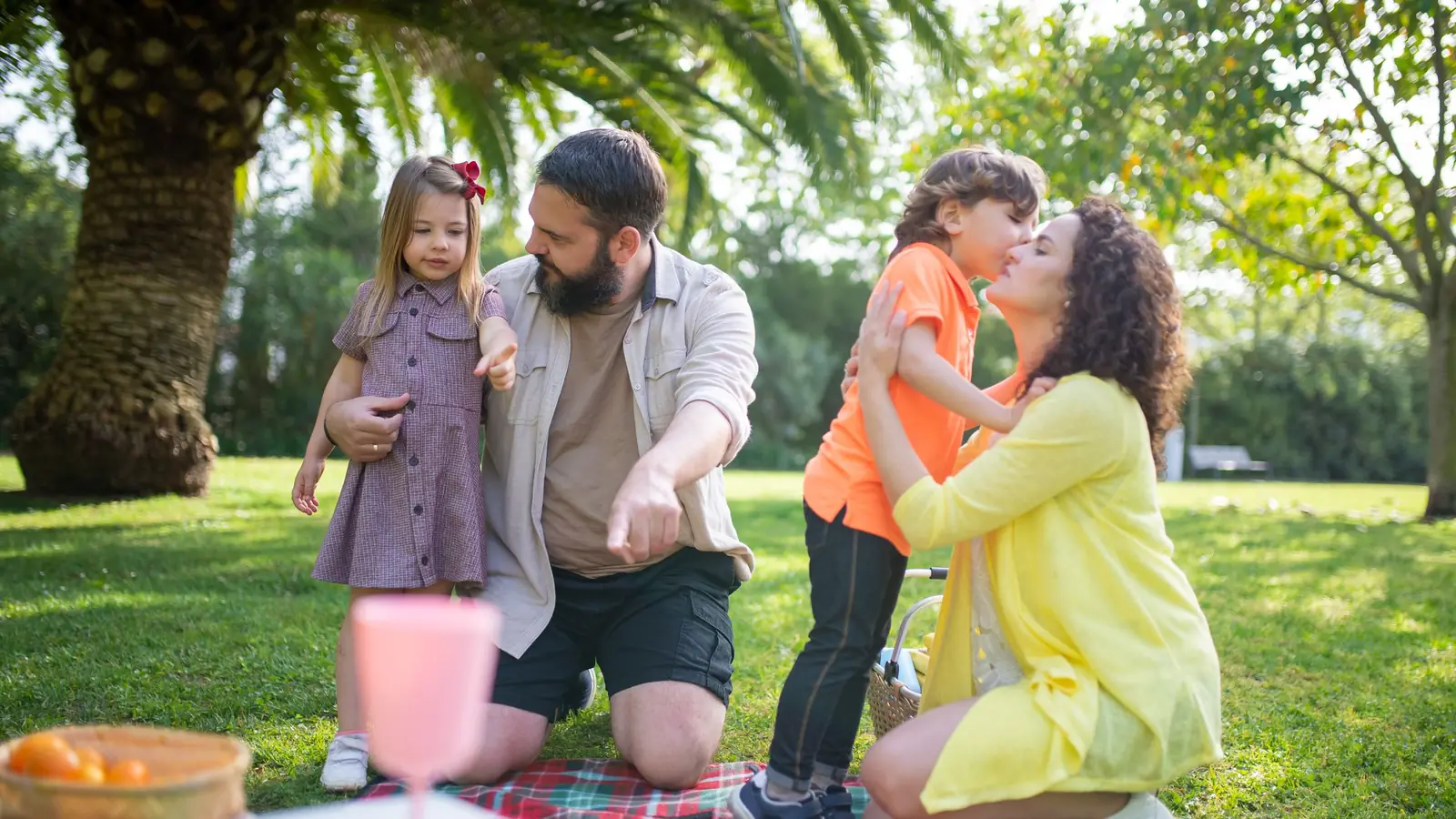 Mom, dad, son and young daughter sharing a hug during a picnic on the grass under palm trees