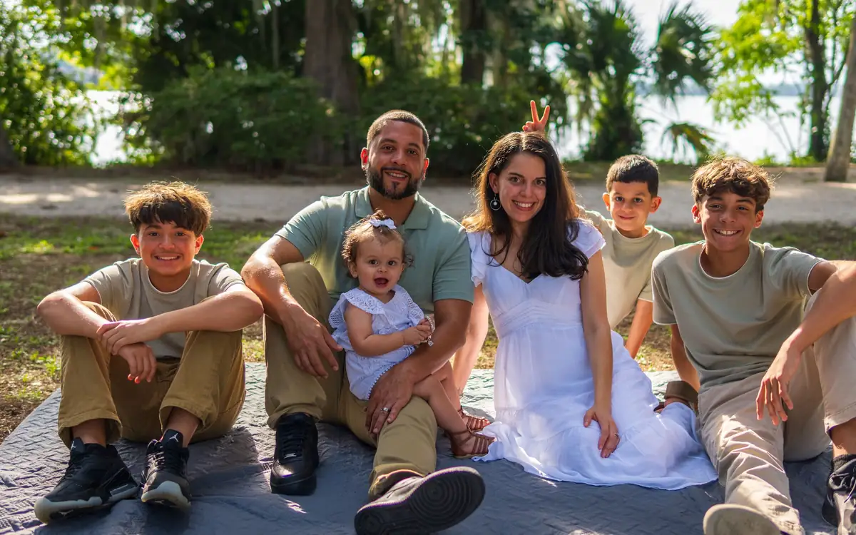 Smiling family of seven sitting together on a picnic blanket in a Florida lakeside park