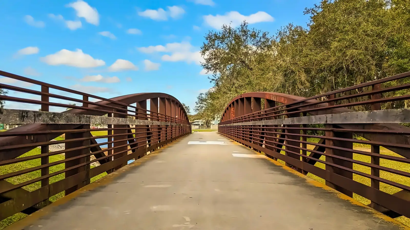 Wooden trail bridge with rust-colored railings at a park in Kissimmee under a blue sky
