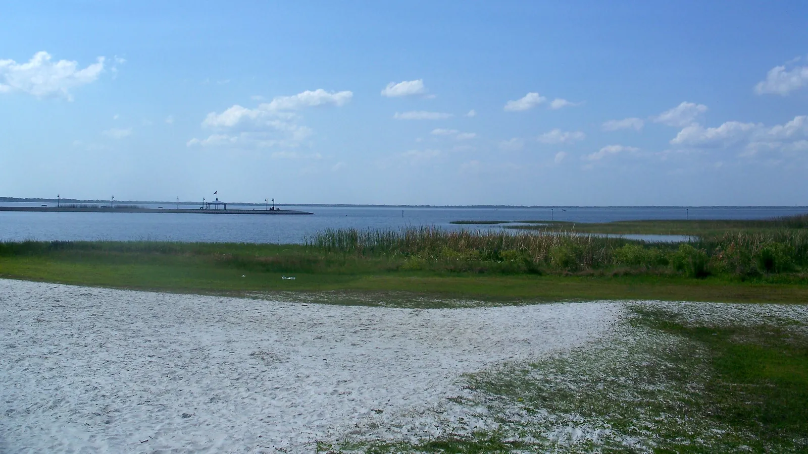 Sandy shore along East Lake Toho in St. Cloud, with a pier in the distance