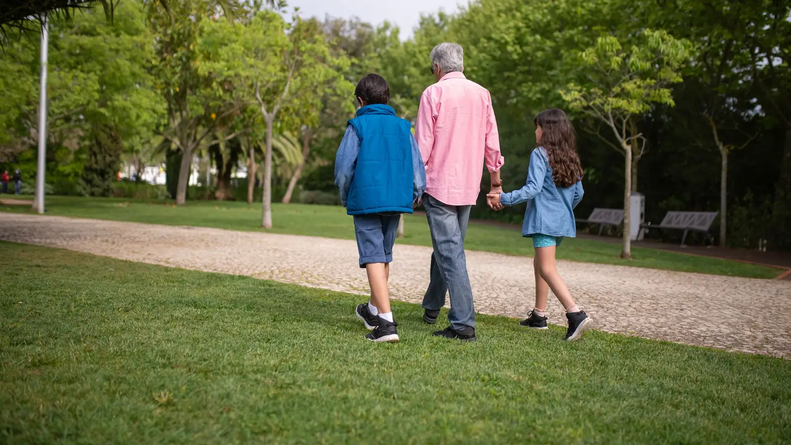 Grandfather walking hand in hand with his two grandchildren along a park path