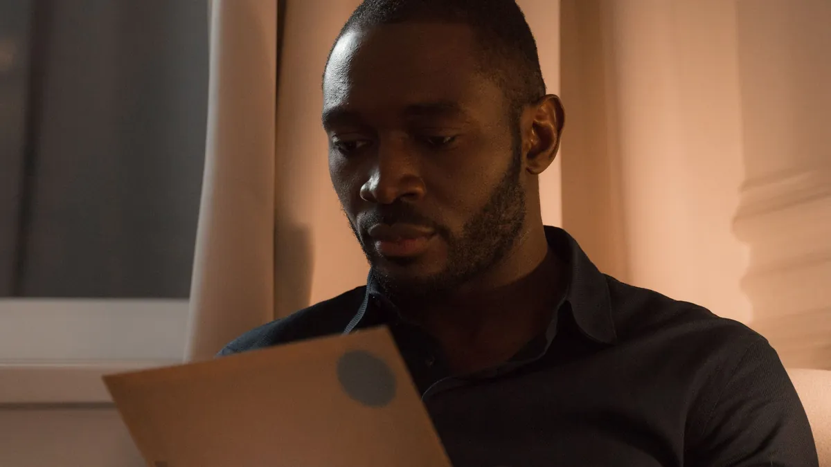 Man sitting by a window at home, reading a letter