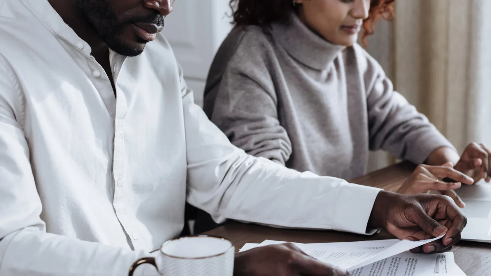 Couple at a table at home going over paperwork, with a laptop open beside them