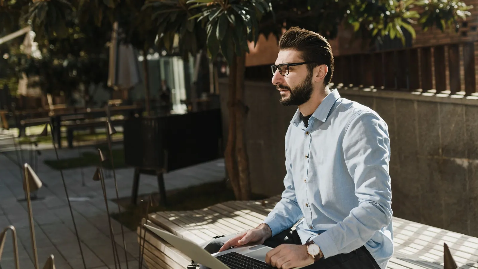 Man working on a laptop on an outdoor bench on a sunny day