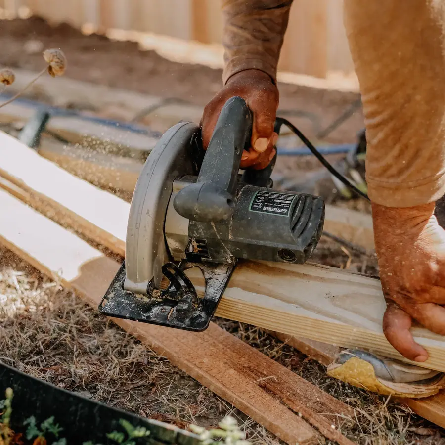 Carpenter cutting wood planks with a circular saw outside