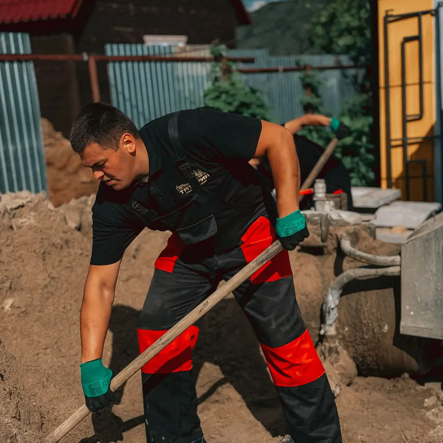 Construction worker in safety gear shoveling sand at a work site