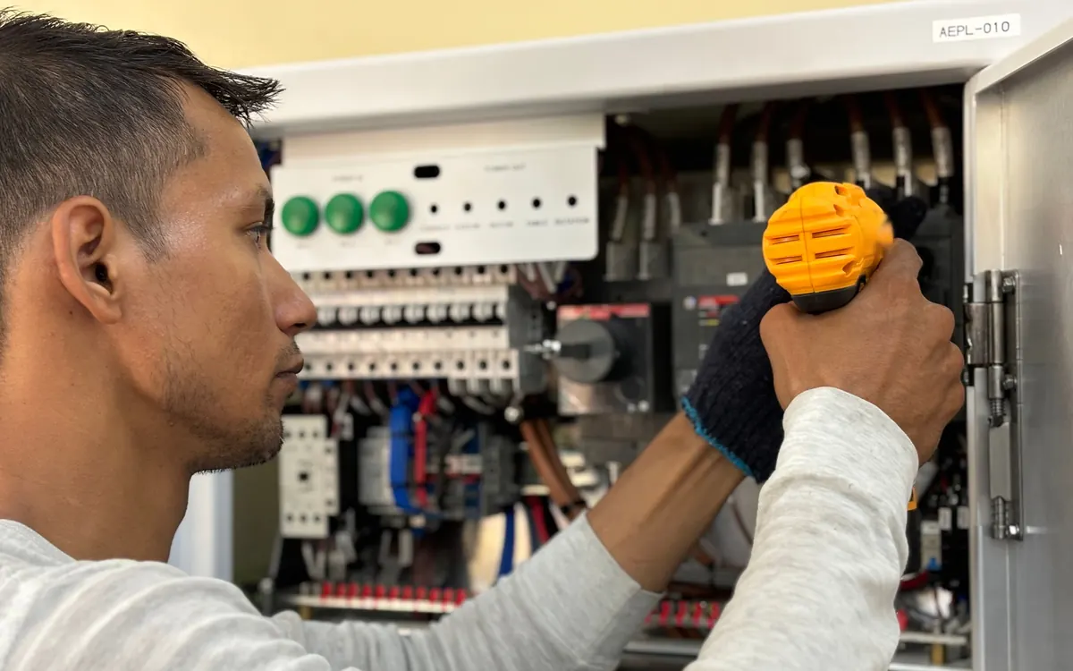 Electrician using a cordless drill to work inside an electrical control panel