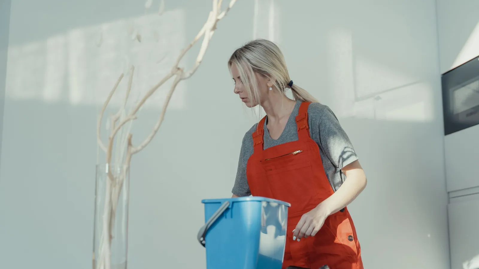 House cleaner in a red apron wiping a counter beside a blue bucket