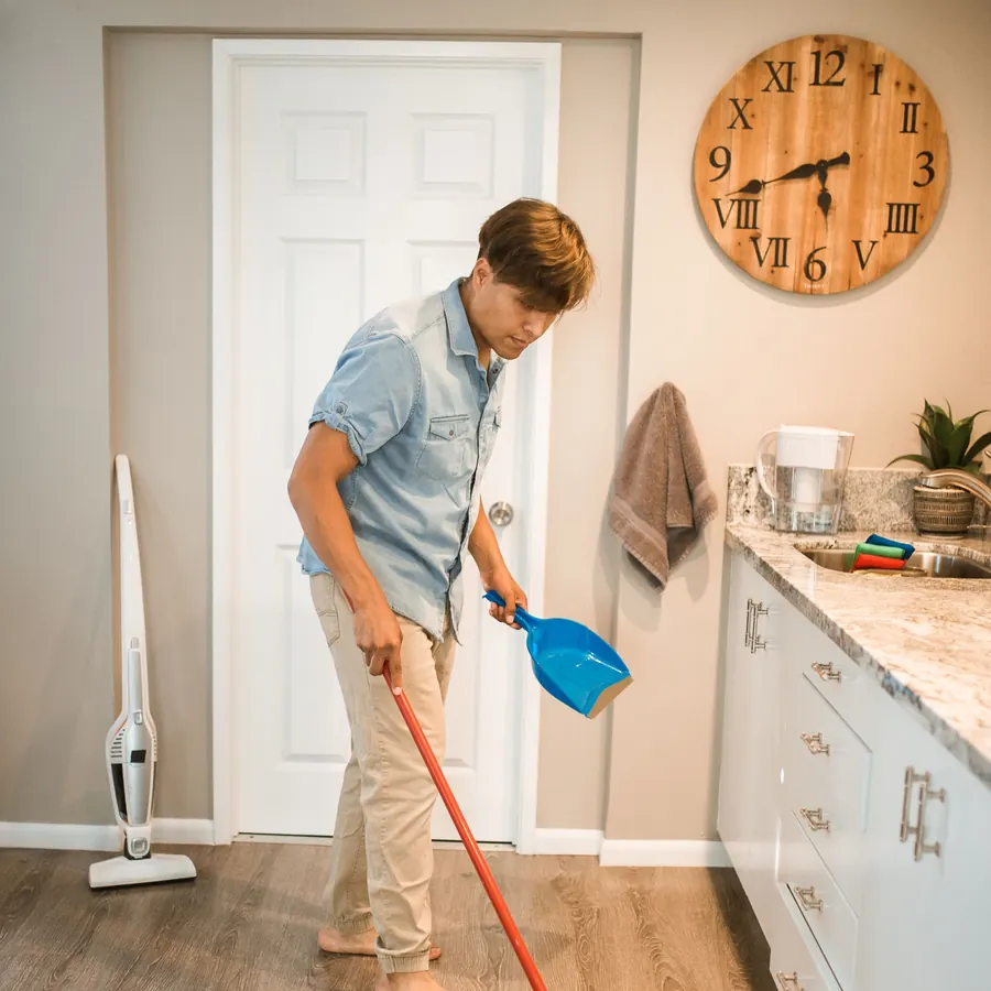 Cleaner sweeping a kitchen floor with a broom and dustpan