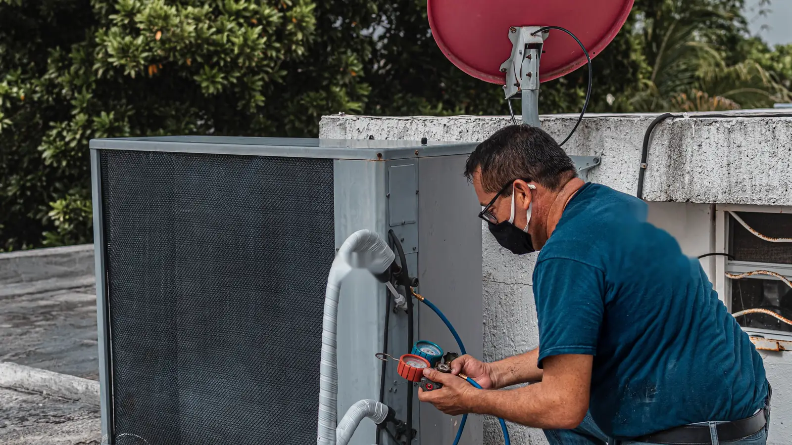 HVAC technician checking refrigerant pressure with a gauge set on a rooftop air conditioning unit