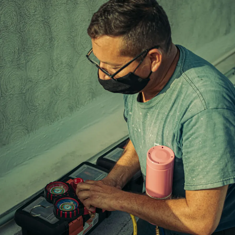 HVAC technician kneeling on a rooftop, reading a manifold gauge set beside his toolbox