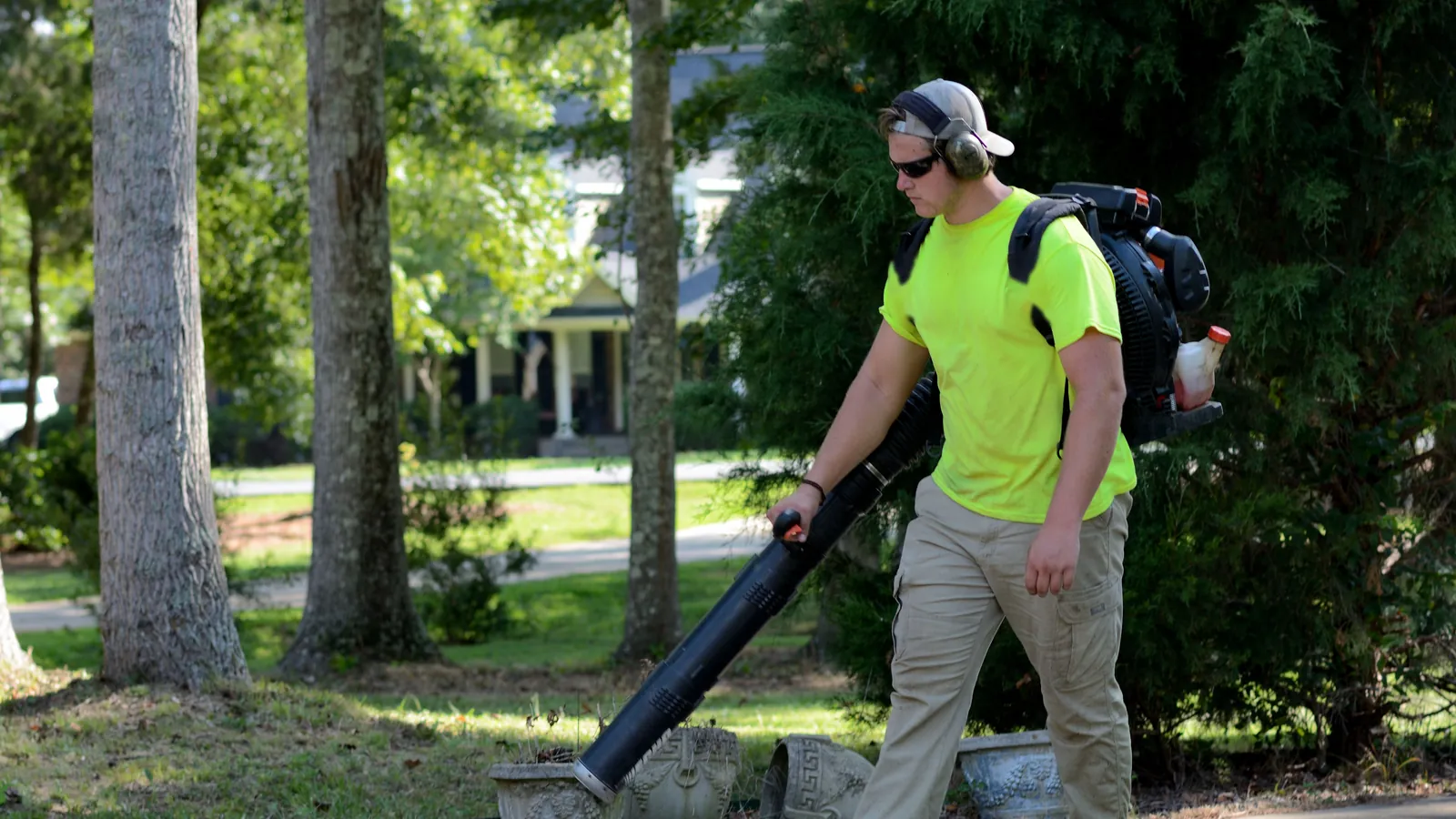 Landscaper wearing ear protection and safety glasses using a backpack leaf blower on a residential street