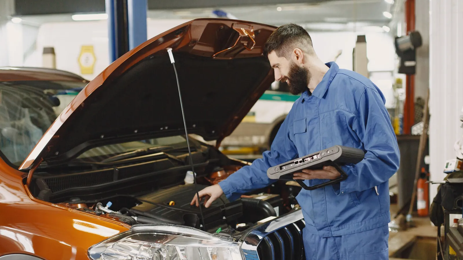 Mechanic in blue coveralls checking an engine with a tablet