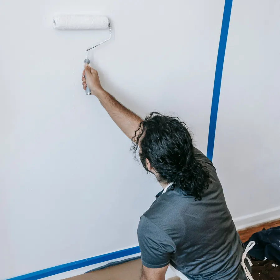 Painter rolling white paint on a wall near the floor