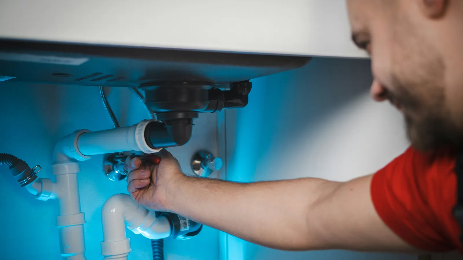 Plumber tightening the drain pipe under a kitchen sink