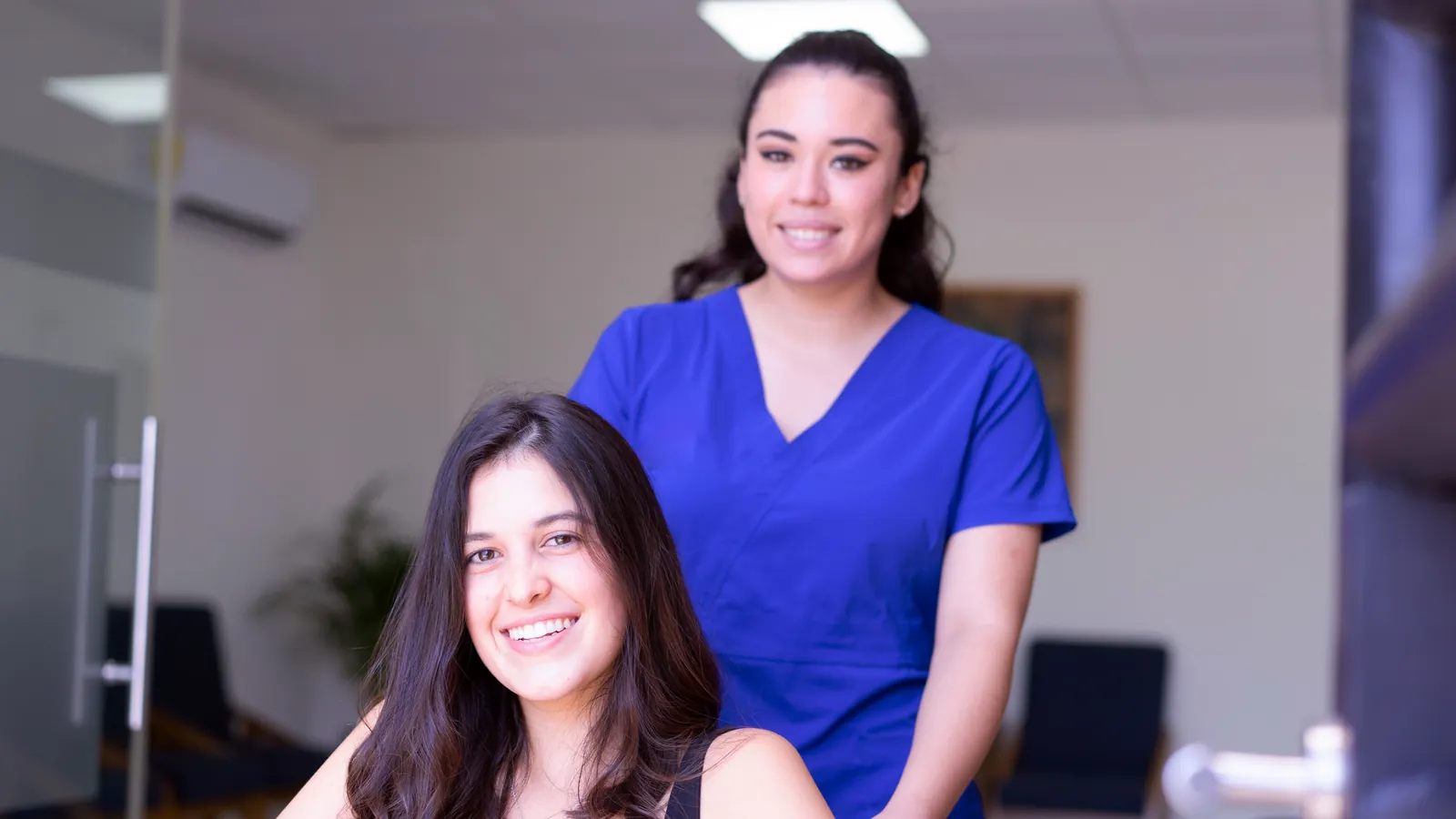 Smiling nurse in blue scrubs helping a patient in a wheelchair