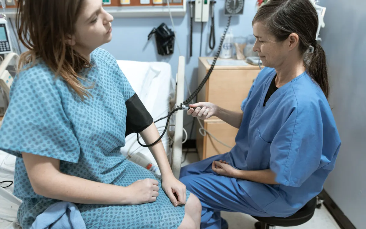 Nurse in scrubs checking a patient's blood pressure in a hospital room