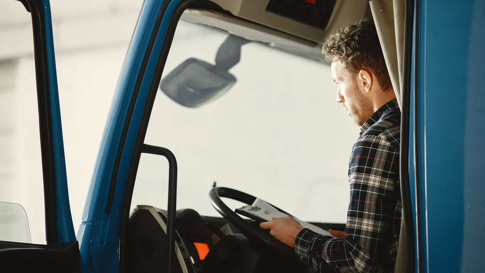 Truck driver in a plaid shirt reading paperwork in his cab