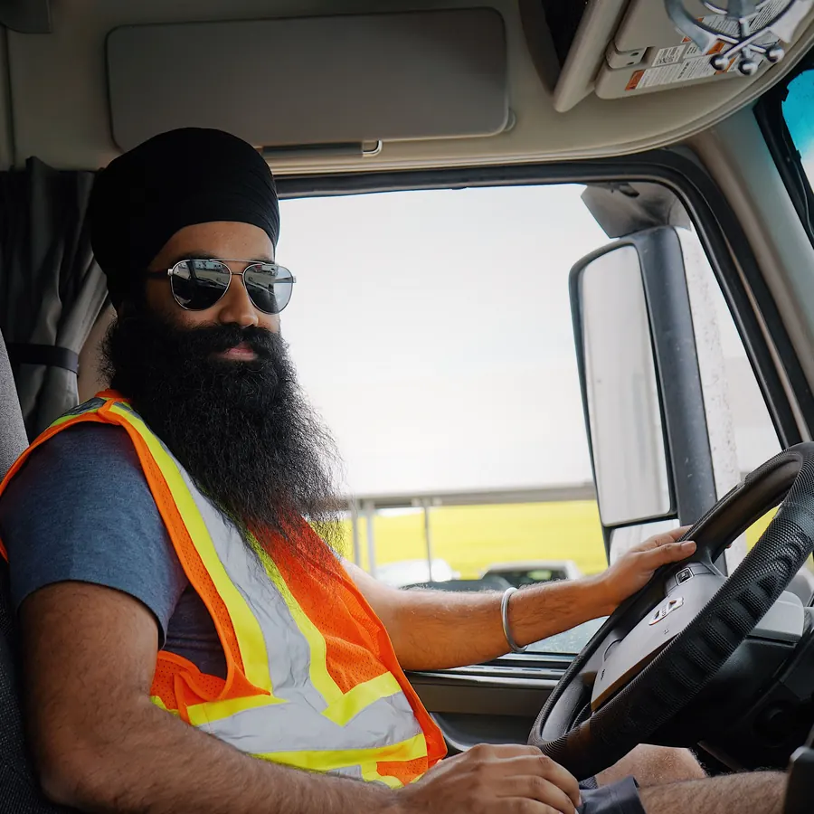Truck driver in a safety vest holding the steering wheel in his cab