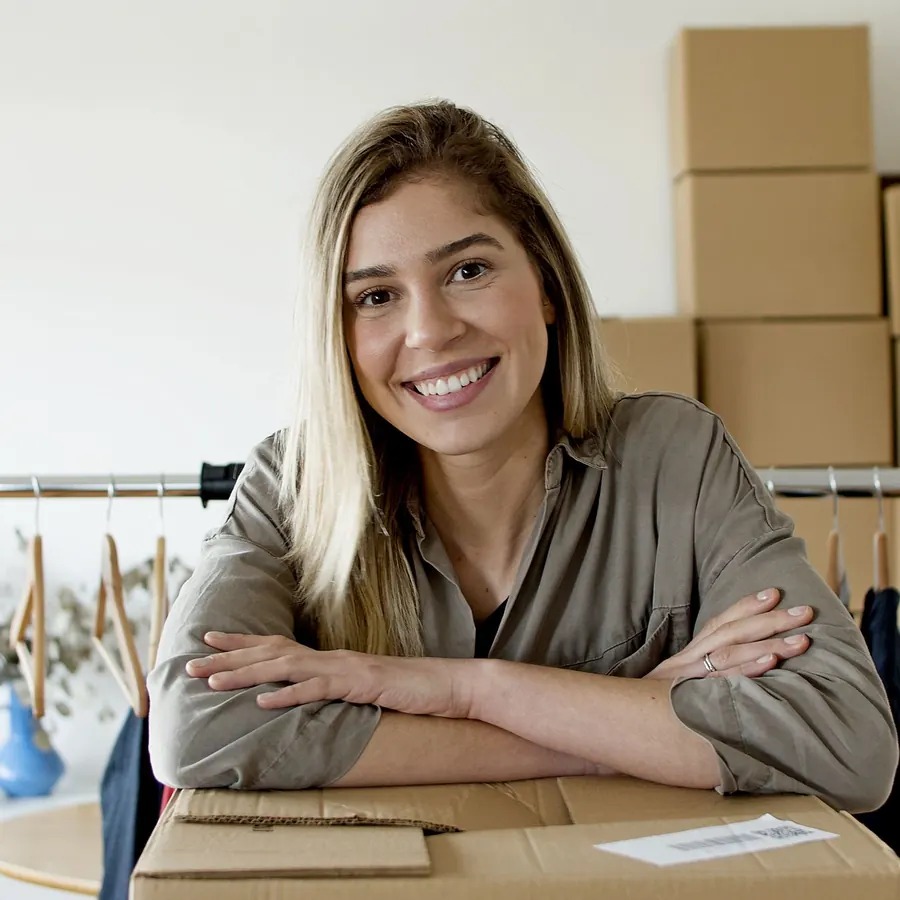 Smiling small business owner sitting with arms folded beside stacked shipping boxes