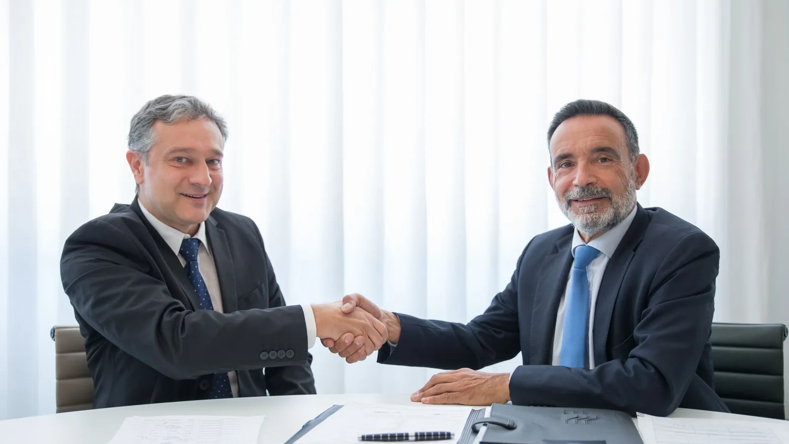 Two business partners shaking hands across a desk