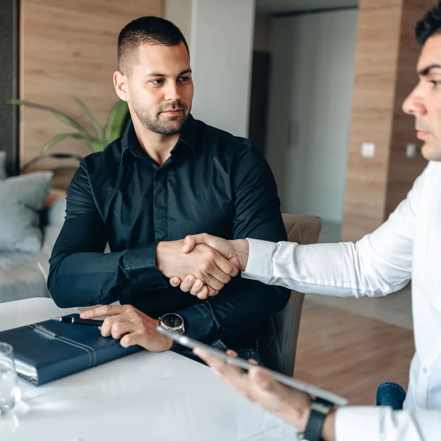 Two men shaking hands over a table with papers and a tablet