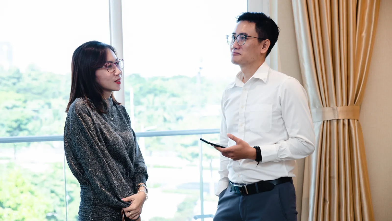 Two coworkers talking by a large office window