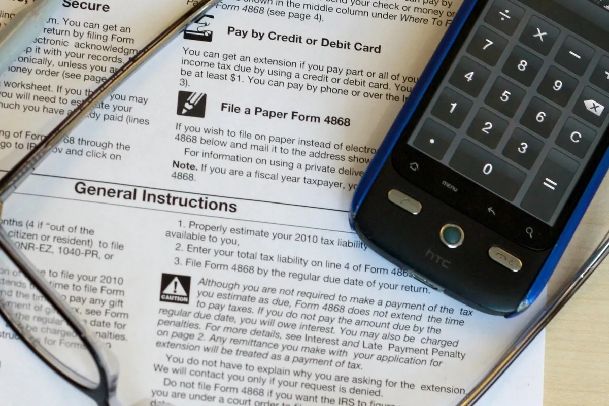 A tax form on a desk with reading glasses and a phone showing a calculator.