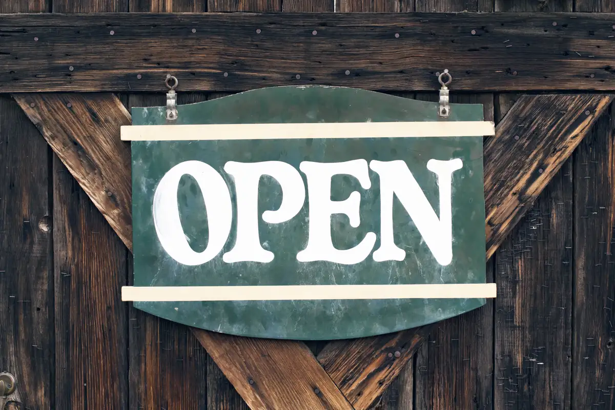 A green and white OPEN sign hanging on a weathered wooden door.
