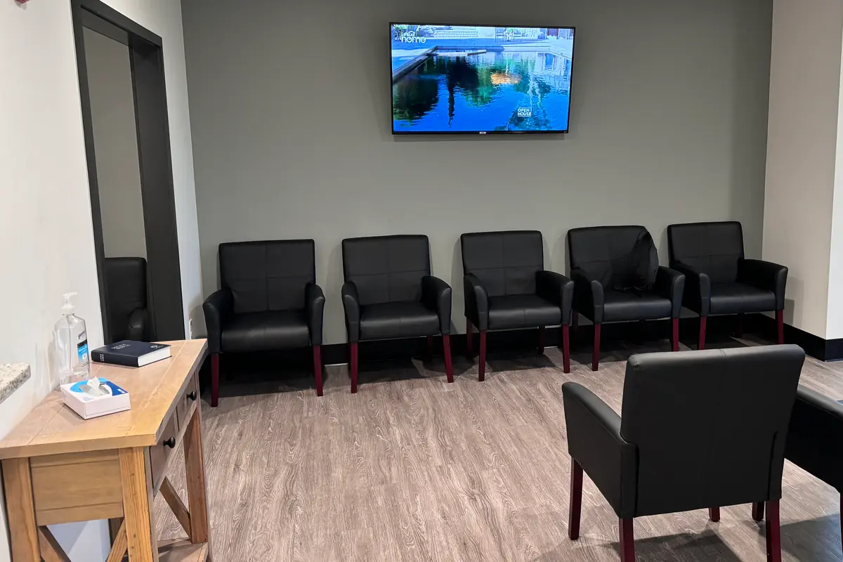 An empty doctor's office waiting room with rows of black chairs and a TV on the wall.