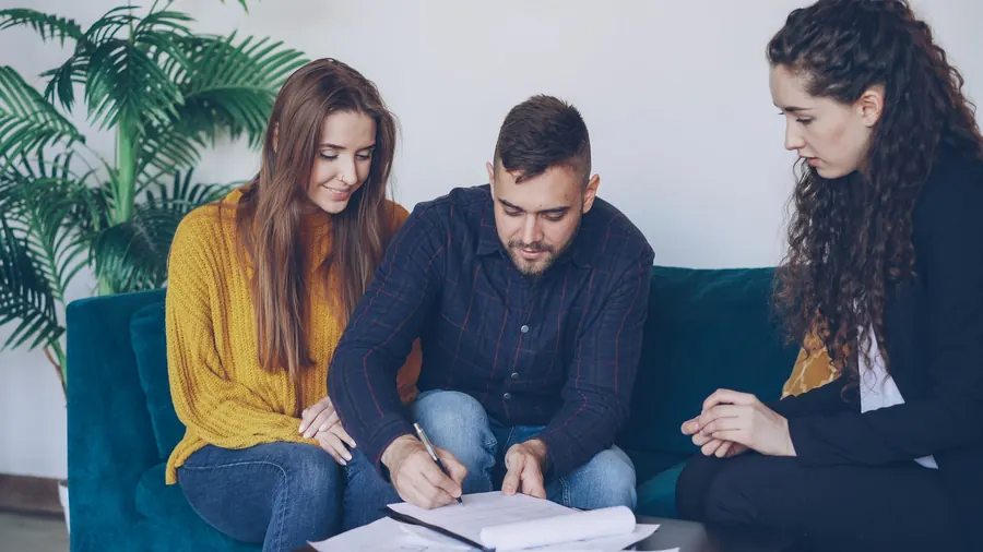Couple signing papers on a sofa while an advisor looks on