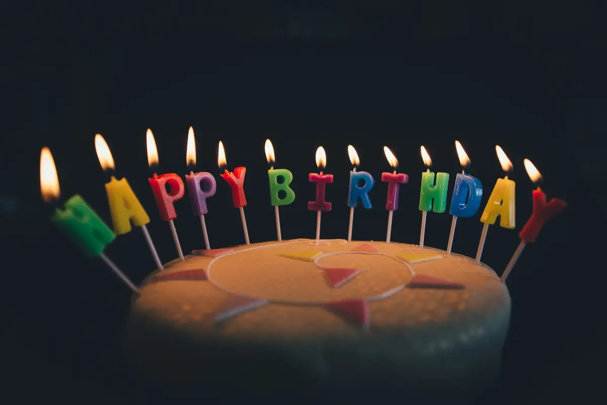 Lit candles spelling Happy Birthday on top of a frosted cake against a dark background.